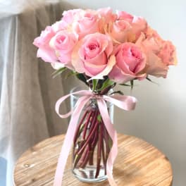 Pink rose bouquet in a clear glass vase with a pink ribbon