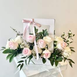 Pink and white roses arranged in a white gift box with a pink ribbon