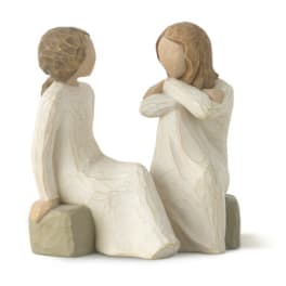 Two carved figurines of girls in cream dresses sitting together