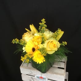 Yellow floral arrangement in a green vase with roses and daisies