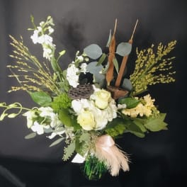 Mixed floral arrangement in a green vase with white blooms and tall seed heads