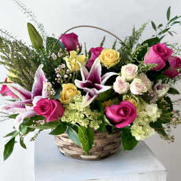 Basket arrangement of pink and yellow roses with white lilies
