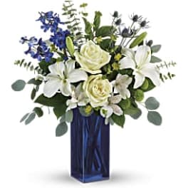 White lilies and roses in a tall blue vase with blue flowers