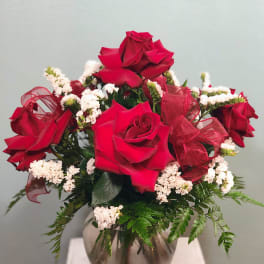 Red roses arranged in a glass vase with white filler flowers and a red ribbon