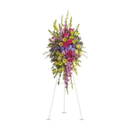 Tall standing spray of pink roses, yellow daisies, and purple flowers on a white easel