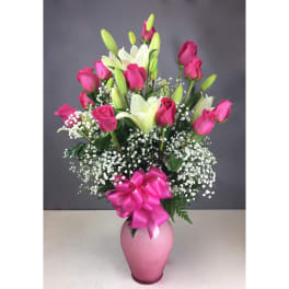 Pink roses and white lilies in a pink vase with a ribbon