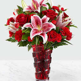 Red roses and pink lilies arranged in a red glass vase