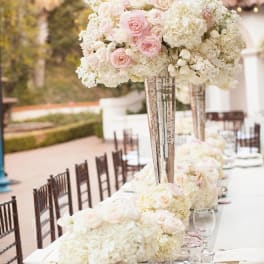 Tall centerpiece of pale pink roses and white flowers in a mirrored vase