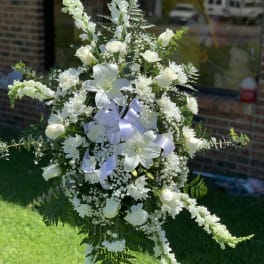 White funeral spray with lilies, roses, and ribbon on a stand