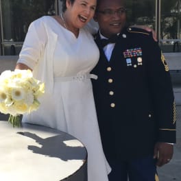 Bride holding a white rose bouquet beside a man in military dress uniform