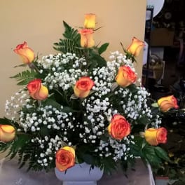 Orange-yellow roses arranged in a white vase with baby's breath