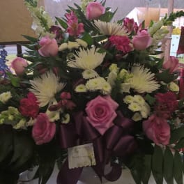 Pink roses and white spider mums arranged in a vase with a purple ribbon.