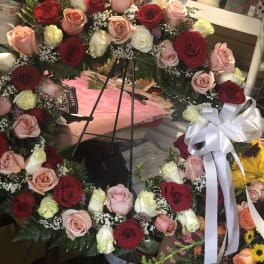 Large circular wreath of red, pink, and white roses with a white ribbon bow