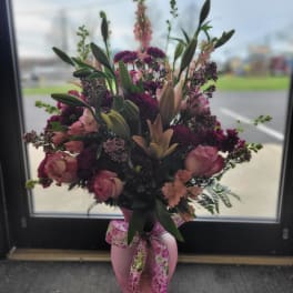 Pink and purple floral arrangement in a pink vase with a ribbon