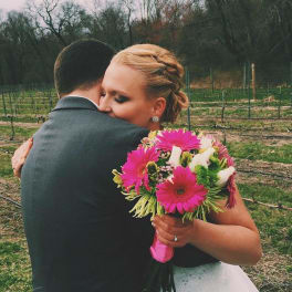 Bride holding a bright pink bouquet while hugging a man outdoors