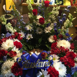 Floral arrangement with red roses, white daisies, and blue flowers with a blue ribbon