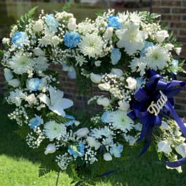 Heart-shaped white floral wreath with blue accents and a purple ribbon