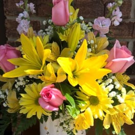 Yellow lilies and pink roses arranged in a white vase