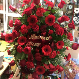 Red roses and gerbera daisies arranged in a standing spray with a "Beloved Aunt" sign.