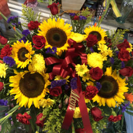 Large bouquet of sunflowers, red roses, and yellow flowers with a red ribbon