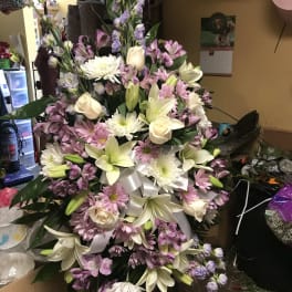 Large pastel floral spray with lilies, roses, daisies, and purple filler flowers