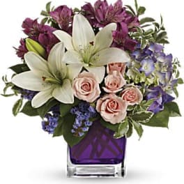 Bouquet of white lilies, pink roses, and purple flowers in a square vase