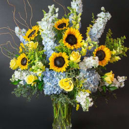 Sunflowers, blue hydrangeas, and yellow roses in a glass vase