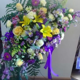 Large standing floral spray with yellow lilies, roses, and purple blooms