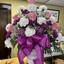 Pink roses and white carnations in a white vase with a purple ribbon