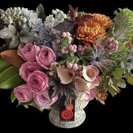 Lush arrangement with pink roses, mini calla lilies, orange mums, blue flowers and ornamental cabbage in a footed vase