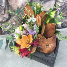 Mixed bouquet with orange lilies and purple flowers in a wooden container