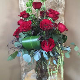 Red roses arranged in a glass vase with mixed greenery