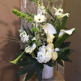 White floral arrangement with calla lilies, roses, and gerbera daisies in a white vase