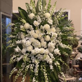 Large white floral standing arrangement with roses, lilies, and cascading blooms