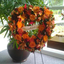 Orange floral wreath on a stand with a ribbon across the center