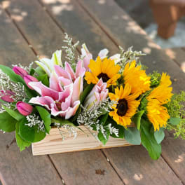 Pink lilies and yellow sunflowers in a wooden box