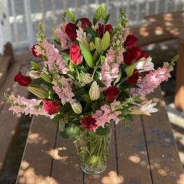 Bouquet of red roses, pink snapdragons, and white lilies in a glass vase