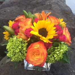 Bouquet of orange roses, pink roses, sunflowers, and green hydrangeas in a glass vase