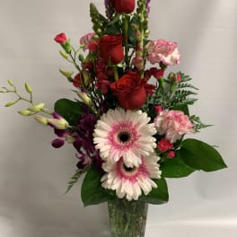 Tall bouquet of red roses, pink gerberas, and purple orchids in a glass vase