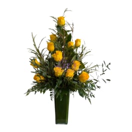 Yellow roses in a tall green vase with mixed greenery