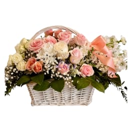 Basket of pink and cream roses with white filler flowers and a peach ribbon