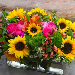 Bright bouquet of sunflowers, pink roses, and orange blooms in a glass vase