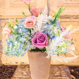 Pink and purple roses with blue hydrangeas in a beige vase