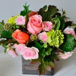 Pink and coral roses arranged in a square wooden vase