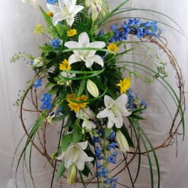 Tall floral arrangement with white lilies, blue flowers, and yellow accents on a stand