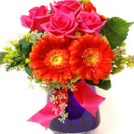 Bouquet of pink roses and orange gerbera daisies in a purple vase