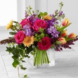 Bouquet of pink roses, purple flowers, and yellow blooms in a clear vase