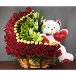Basket of red roses with lilies, chocolates, and a teddy bear holding a heart