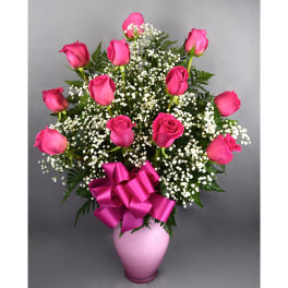 Pink roses in a pink vase with baby's breath and a ribbon bow