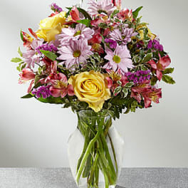 Mixed bouquet of yellow roses, pink daisies, and alstroemeria in a clear vase